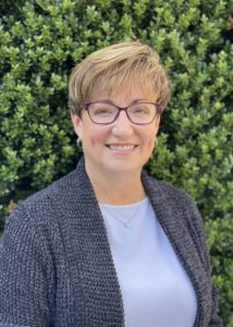 Kathleen Smith con camisa azul, jersey gris y gafas moradas